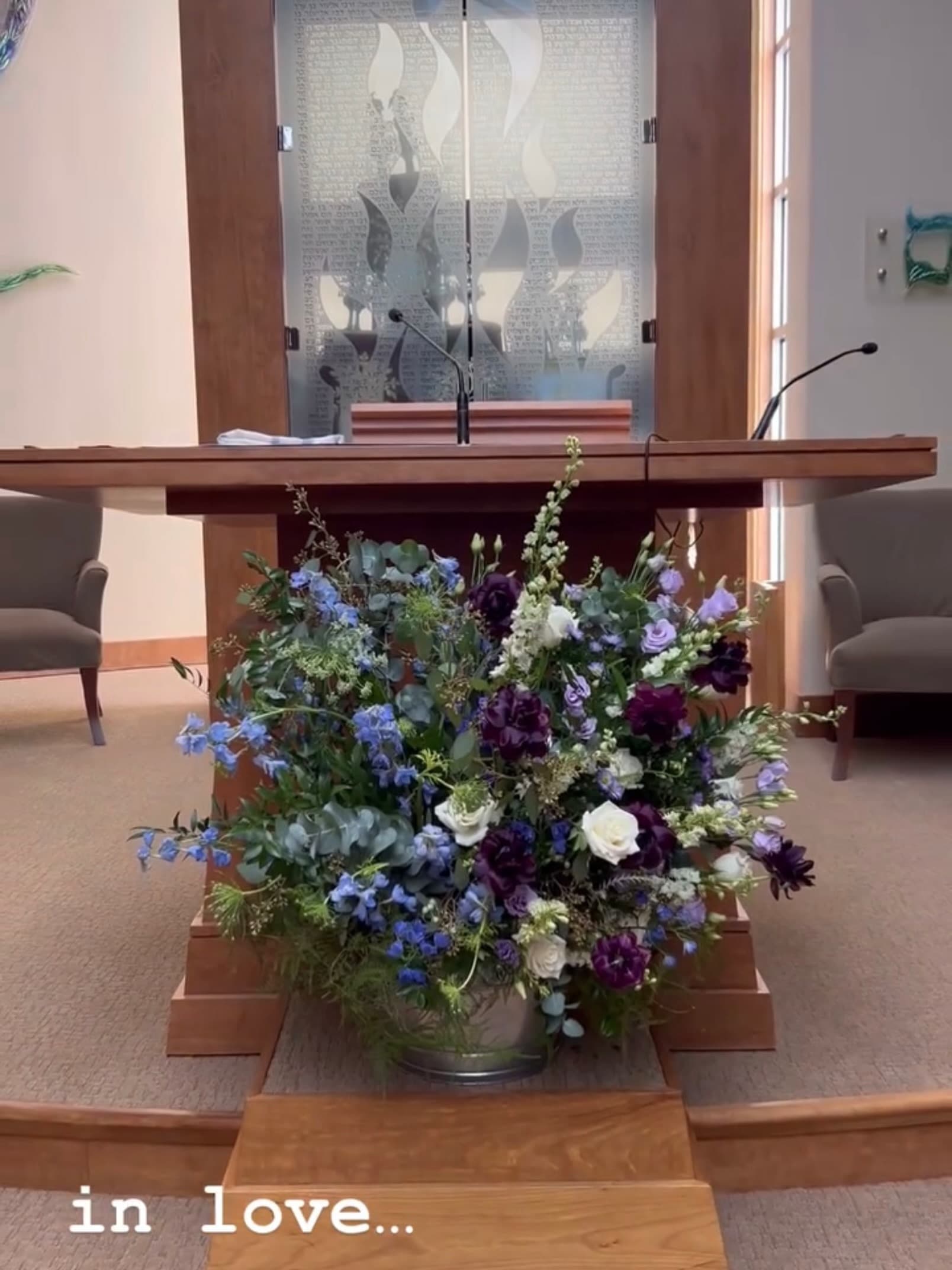 A blue, purple and white arrangement of delphinium, lisianthus and roses at the foot of a synagogue bimah.